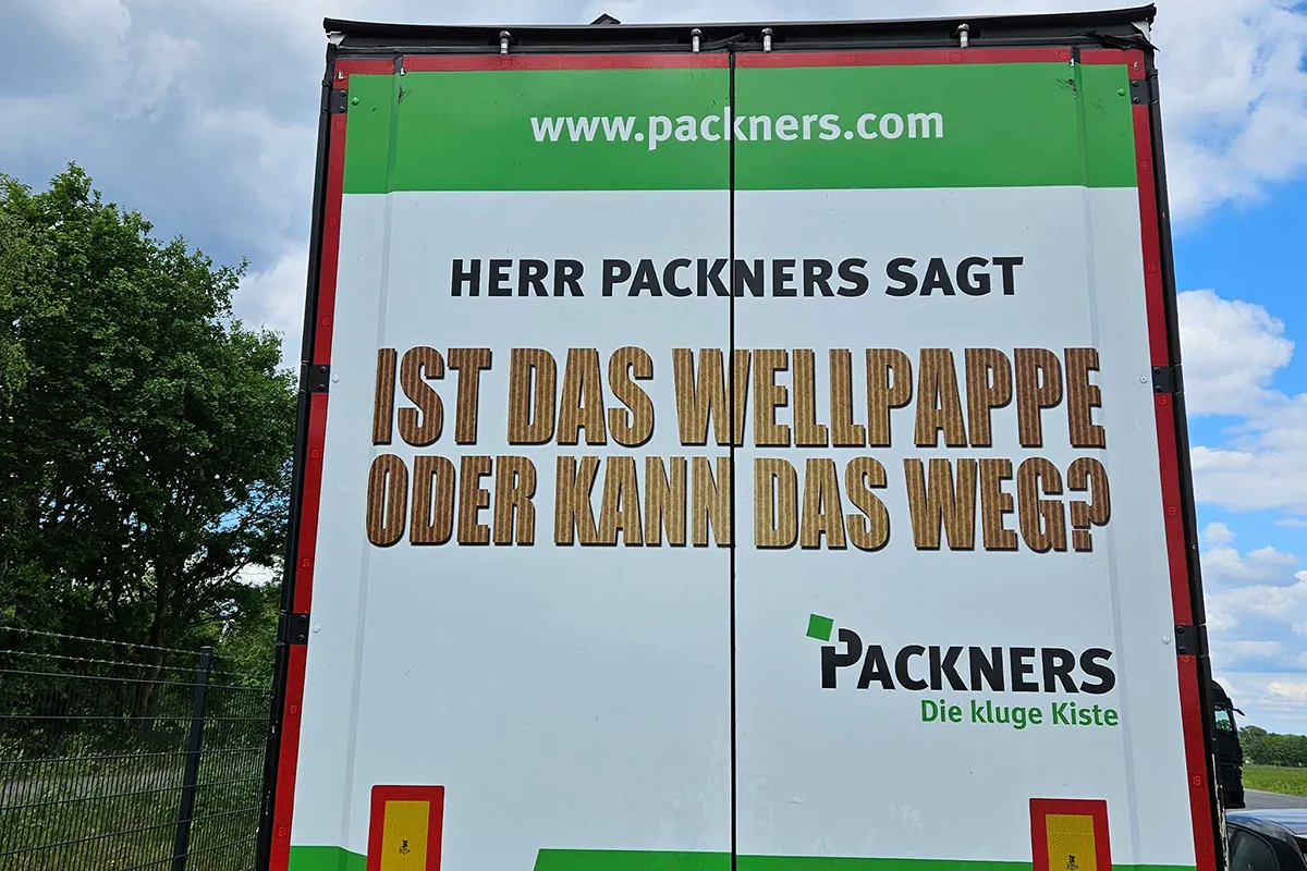 Lkw-Heck mit Aufschrift: Herr Packners sagt: Ist das Wellpappe oder kann das weg? Packners – Die kluge Kiste