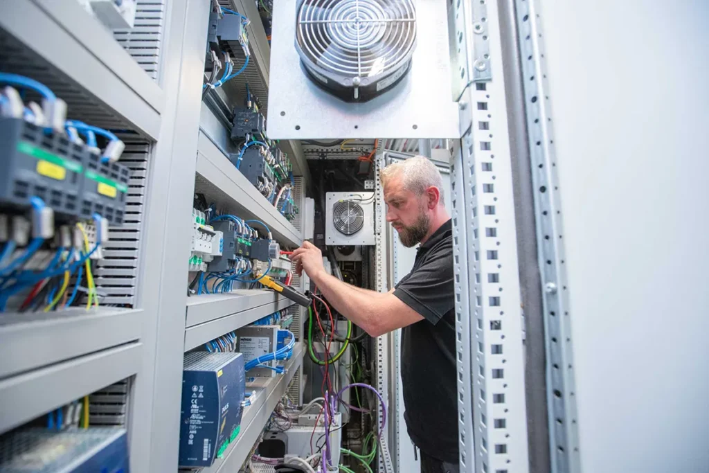 Mitarbeiter prüft elektrische Komponenten in einem geöffneten Schaltschrank