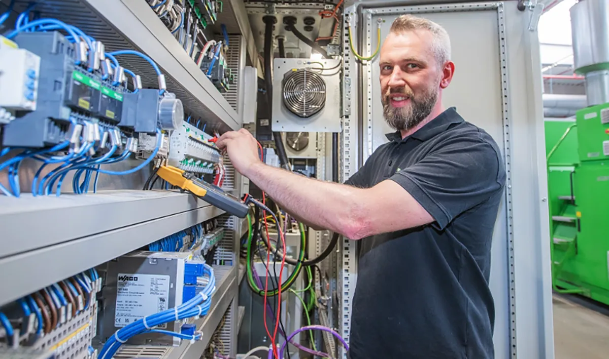 Elektroniker arbeitet an einem geöffneten Schaltschrank und prüft elektrische Komponenten