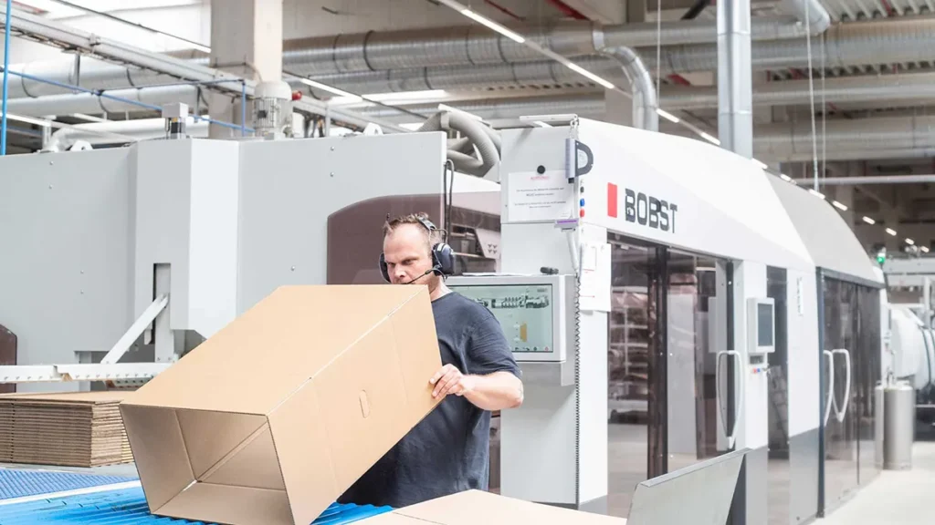 Mitarbeiter faltet einen Karton an einer Produktionsmaschine zur Überprüfung