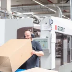 Mitarbeiter faltet einen Karton an einer Produktionsmaschine zur Überprüfung