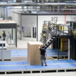 Produktion von Wellpappe mit automatisierter Anlage und Mitarbeiter, der einen Stapel Kartonzuschnitte positioniert