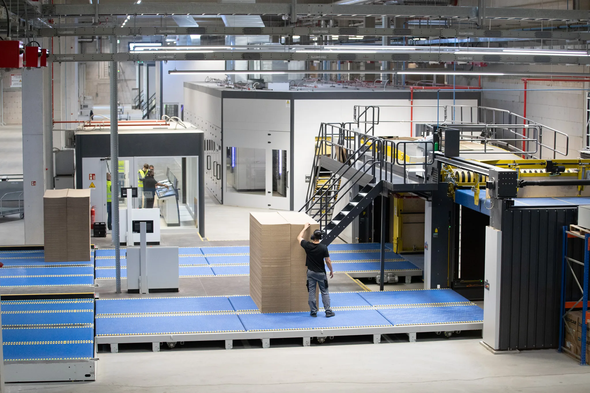 Produktion von Wellpappe mit automatisierter Anlage und Mitarbeiter, der einen Stapel Kartonzuschnitte positioniert
