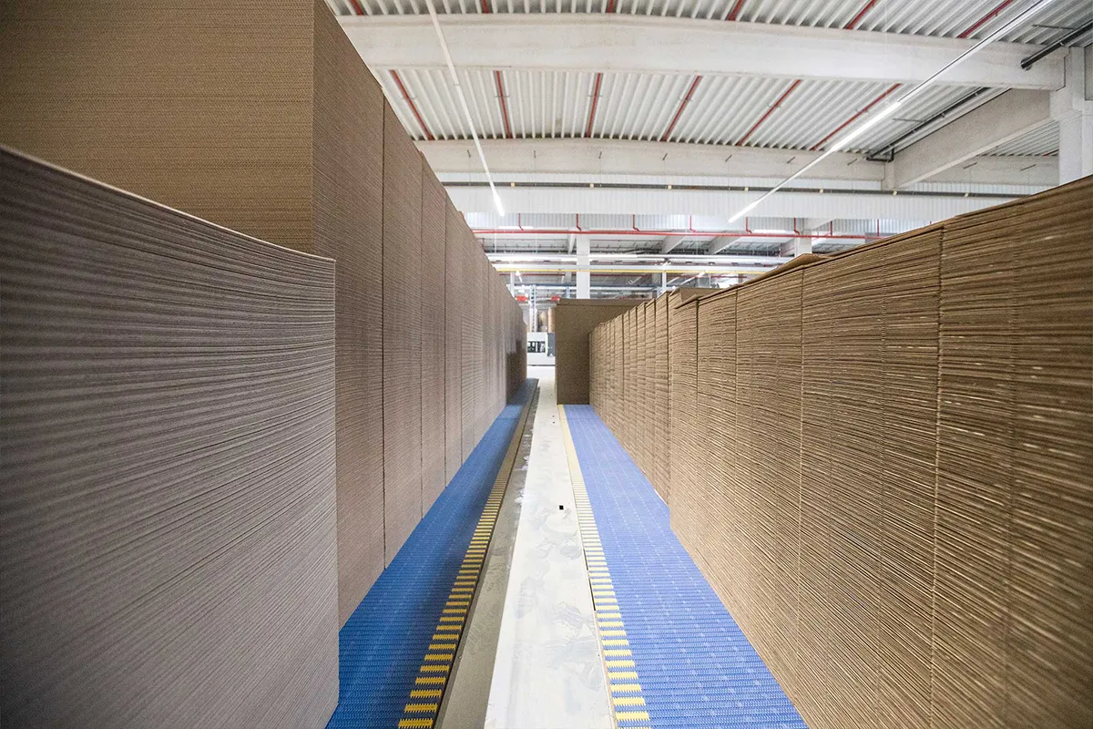 Innenaufnahme: lange Reihen gestapelter Kartonagen/Bogenware in einer Produktionshalle.