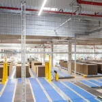 Große Produktionshalle mit Fördertechnik und gestapelten Karton-Bögen auf Paletten.