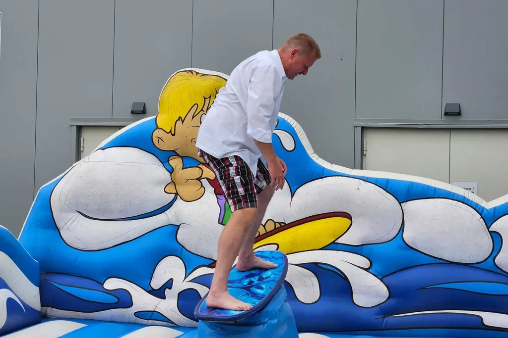 Mitarbeiter balanciert barfuß auf einem Surfbrett auf einer aufblasbaren Wellenattraktion