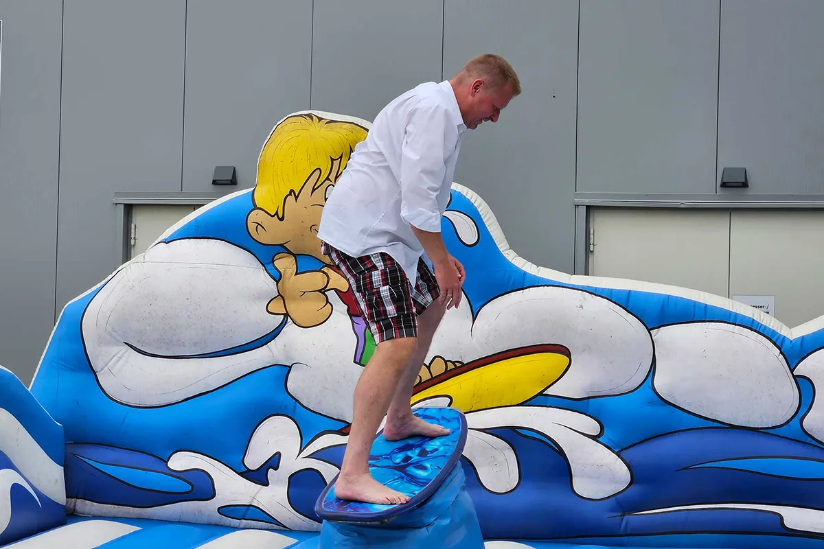 Mitarbeiter balanciert barfuß auf einem Surfbrett auf einer aufblasbaren Wellenattraktion