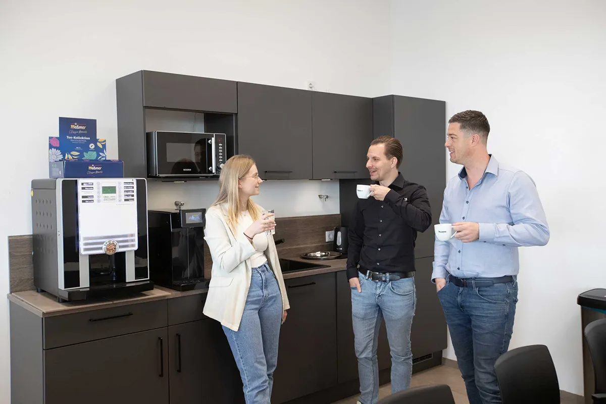 Mitarbeitende stehen in einer Büroküche zusammen und trinken Kaffee