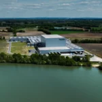 Weite Luftaufnahme des Packners-Werks am Wasser mit umliegenden Feldern.