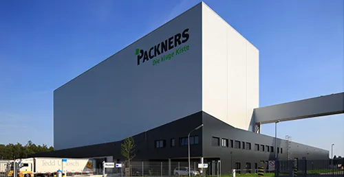 Außenansicht Packners-Gebäude mit großem Logo an der Fassade bei blauem Himmel.